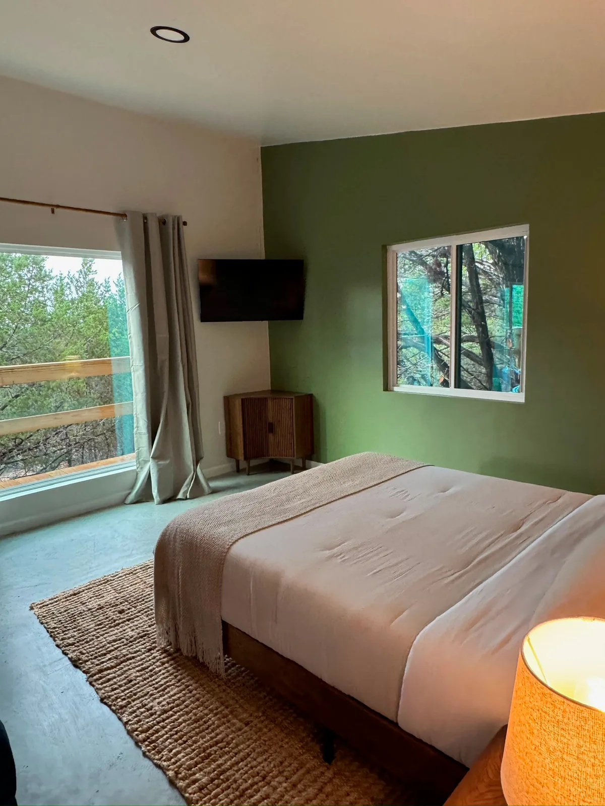 The bed against the green accent wall, with a window onto the trees